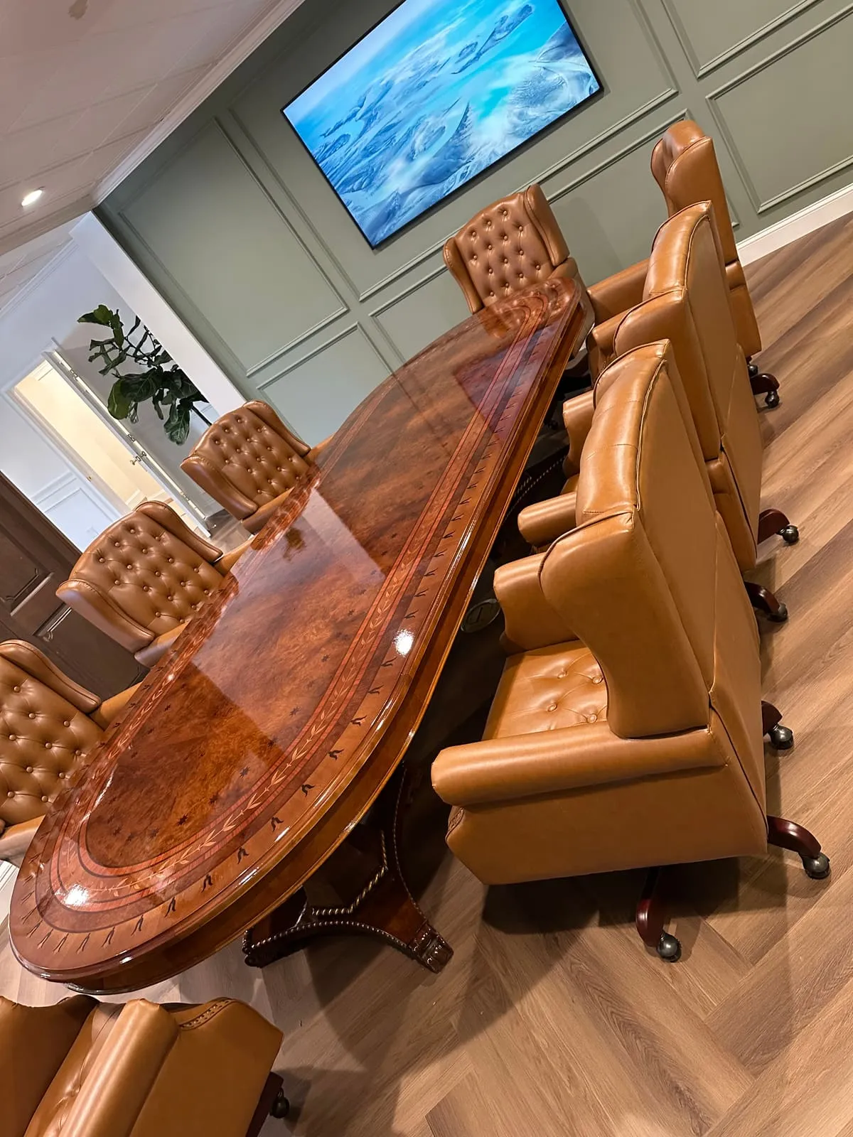 Oval high-gloss table with a burl-figured top surrounded by tan tufted-leather armchairs